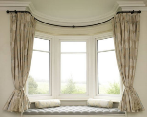 Bay Window With Beige Patterned Curtains And A Cushioned Seating Area, Featuring Two Bolster Pillows.
