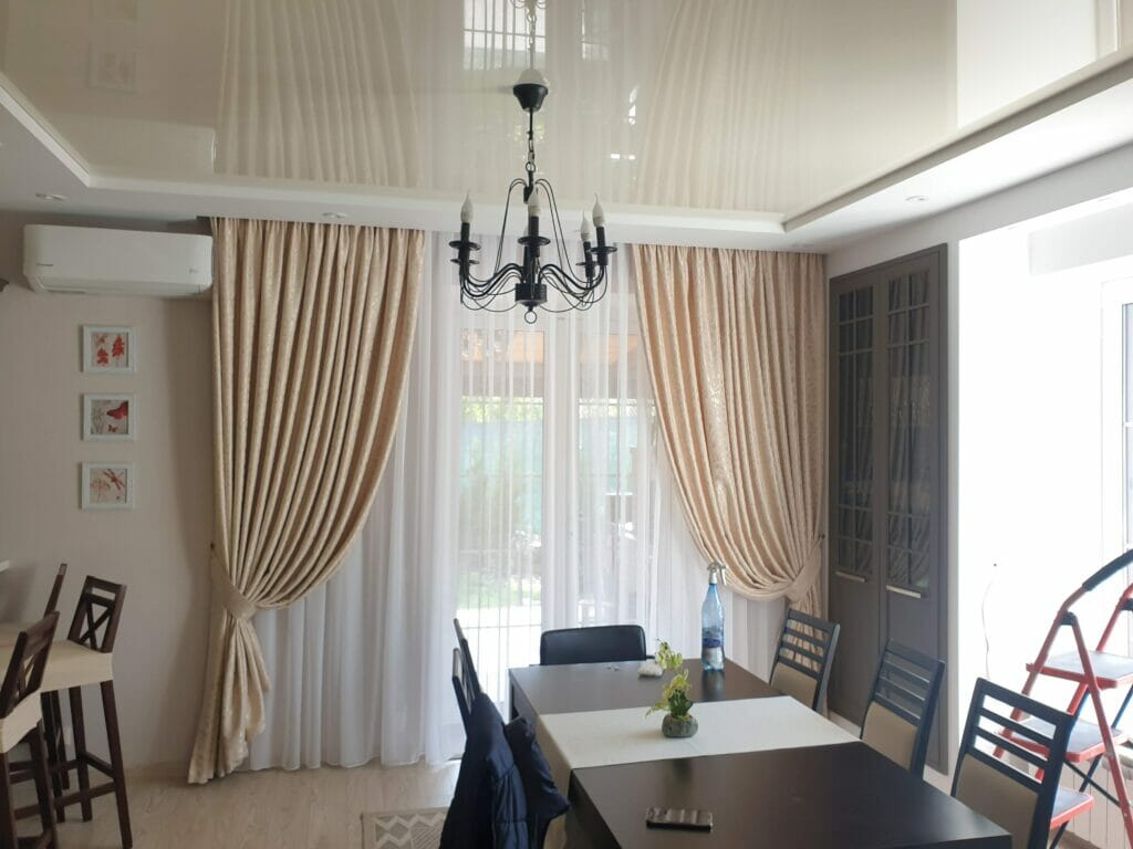 A dining room with beige curtains and a chandelier.